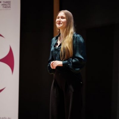 A woman with blonde hair wearing a green blouse and navy pants standing on a stage